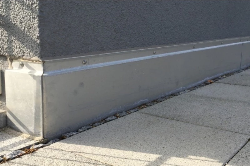 Graues Metall-Sockelblech als Sockelverkleidung an gedämmter Hausfassade, sauber montiert mit Schrauben, schützt Putz vor Spritzwasser und mechanischen Schäden.