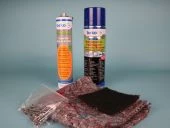 Zwei Sprühdosen stehen neben einem transparenten Beutel mit kleinen Metallteilen. Auf einem Stoffstück und einem dunkel gefärbten Material liegen weitere Materialien. Der Hintergrund ist einheitlich hell.