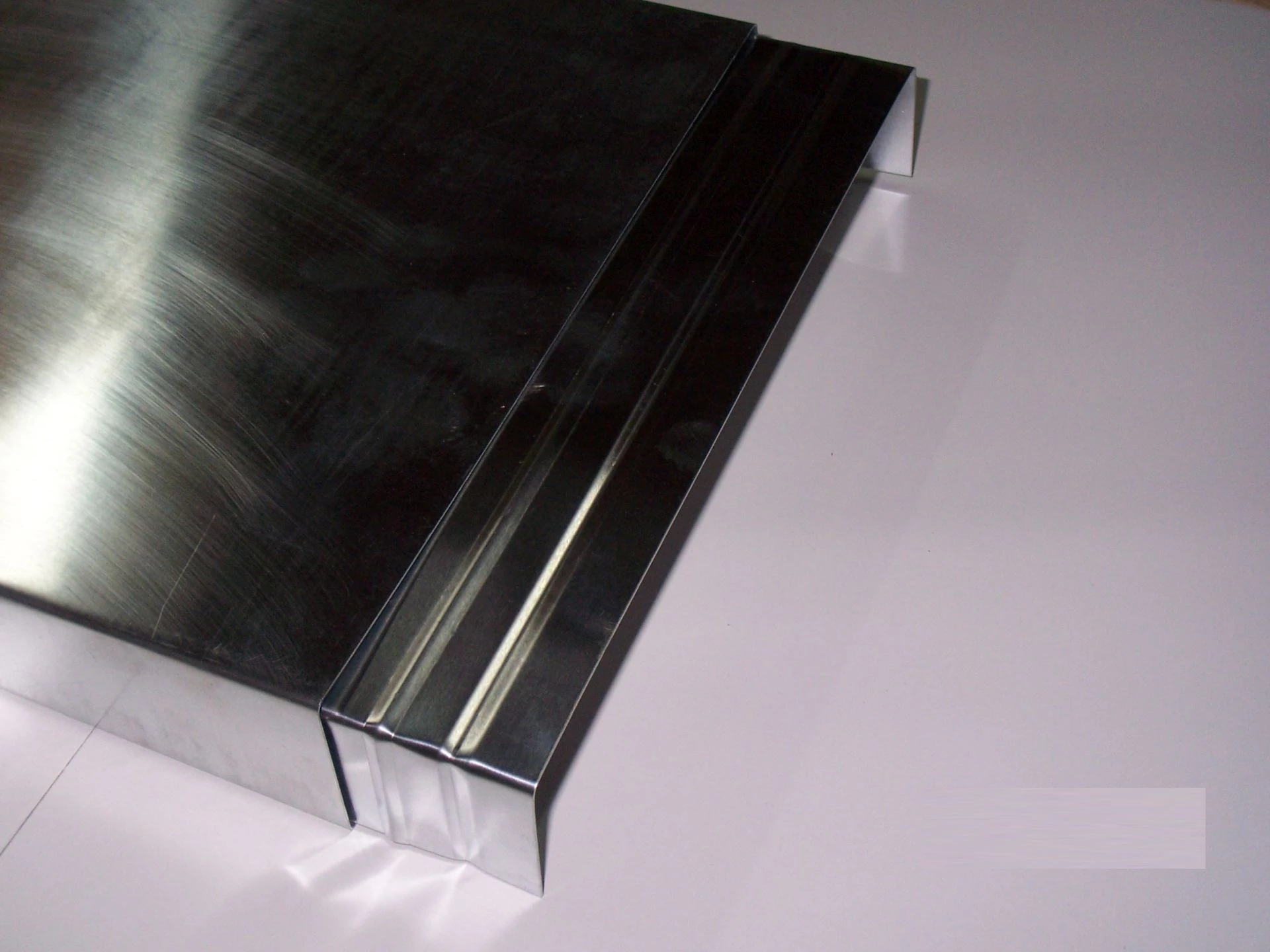Ein glänzendes, rechteckiges Metallprofil mit einer glatten Oberfläche und einem umgebrachten Rand auf einer weißen Unterlage. Es zeigt eine präzise Kante, die zur Montage geeignet ist.