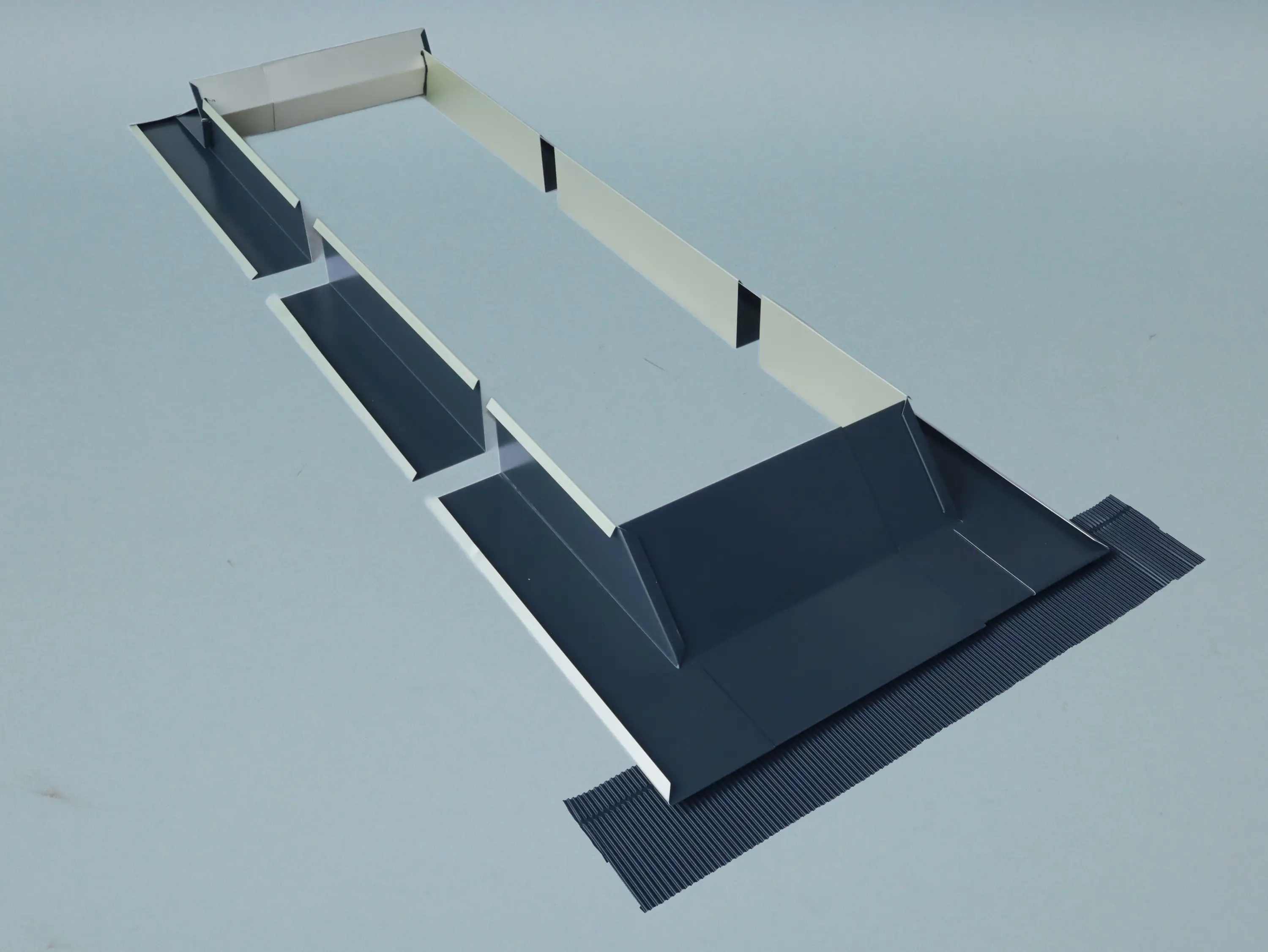 Eine längliche Dachrinne aus metallischen Materialien, mit seitlichen Wandungen und abgerundeten Ecken, zeigt Einlässe für Regenwasser. Sie ist auf einem grauen Hintergrund positioniert.