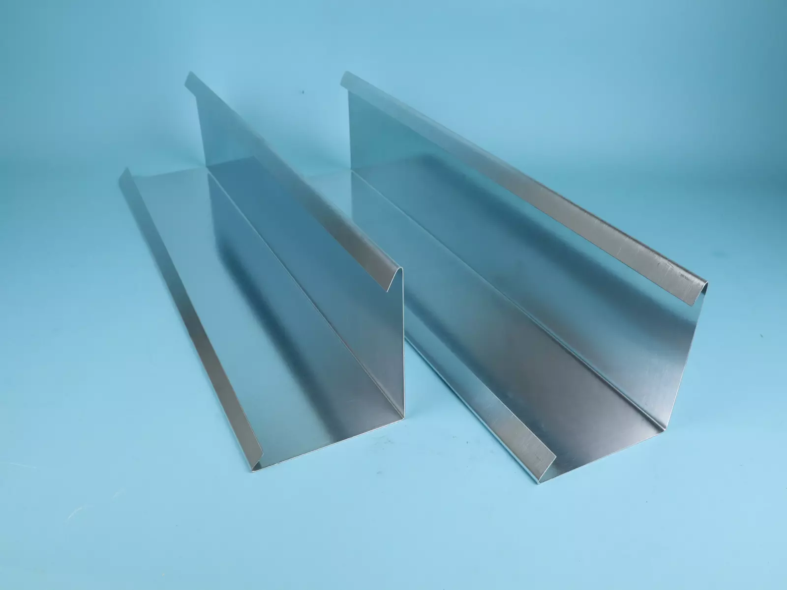 Zwei Aluminiumprofile mit einer angeschrägten Kante sind nebeneinander auf einem blauen Hintergrund angeordnet. Die Profile haben eine glatte, glänzende Oberfläche und sind in unterschiedlichen Längen.