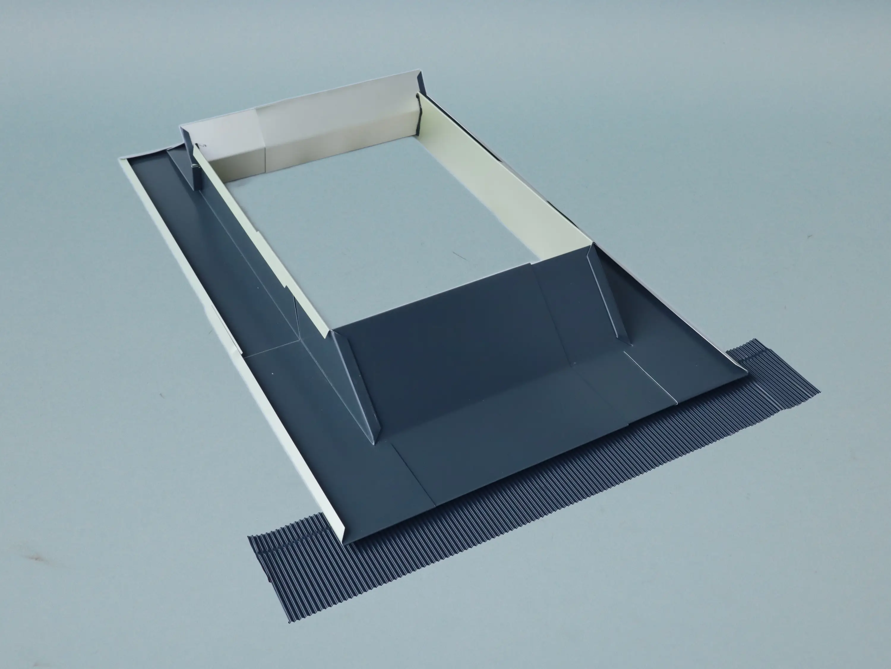 Ein Dachrinnen-System aus grau lackiertem Metall mit einer rechteckigen Form, das am unteren Rand eine strukturierte Oberfläche zeigt. Es ist auf einem einfarbigen Hintergrund platziert.